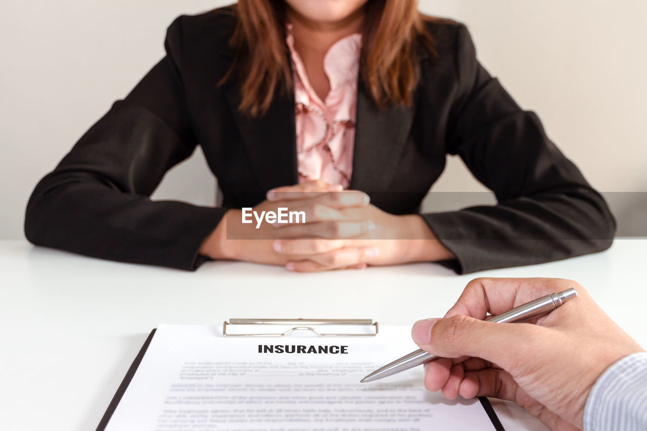 Cropped hand holding pen pointing on insurance contract while explaining to customer in office