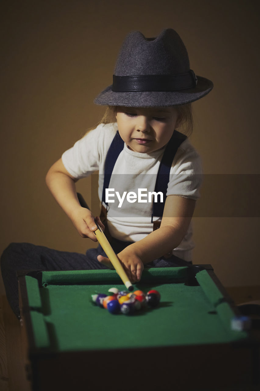 Charming child in retro clothes playing toy billiards.