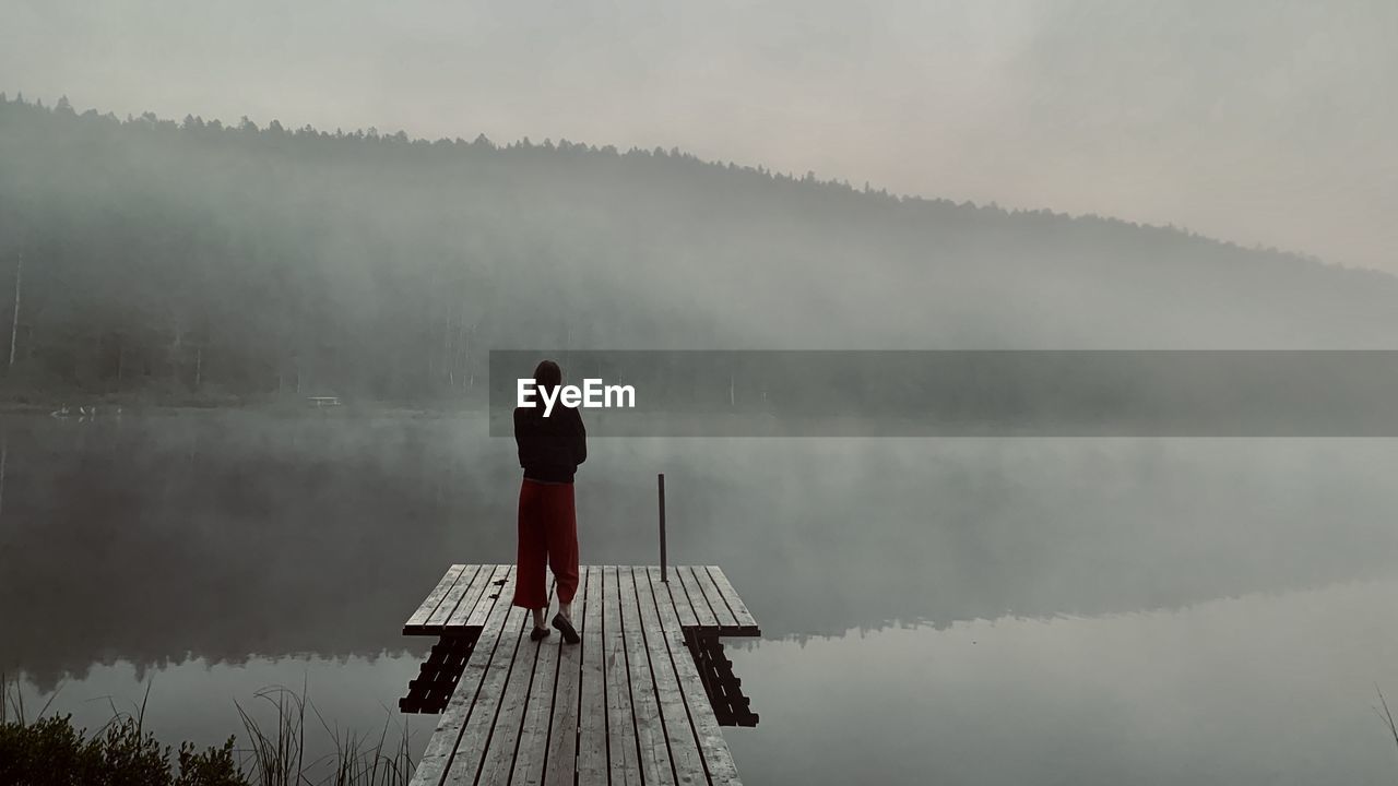 Rear view of girl standing on lake against sky