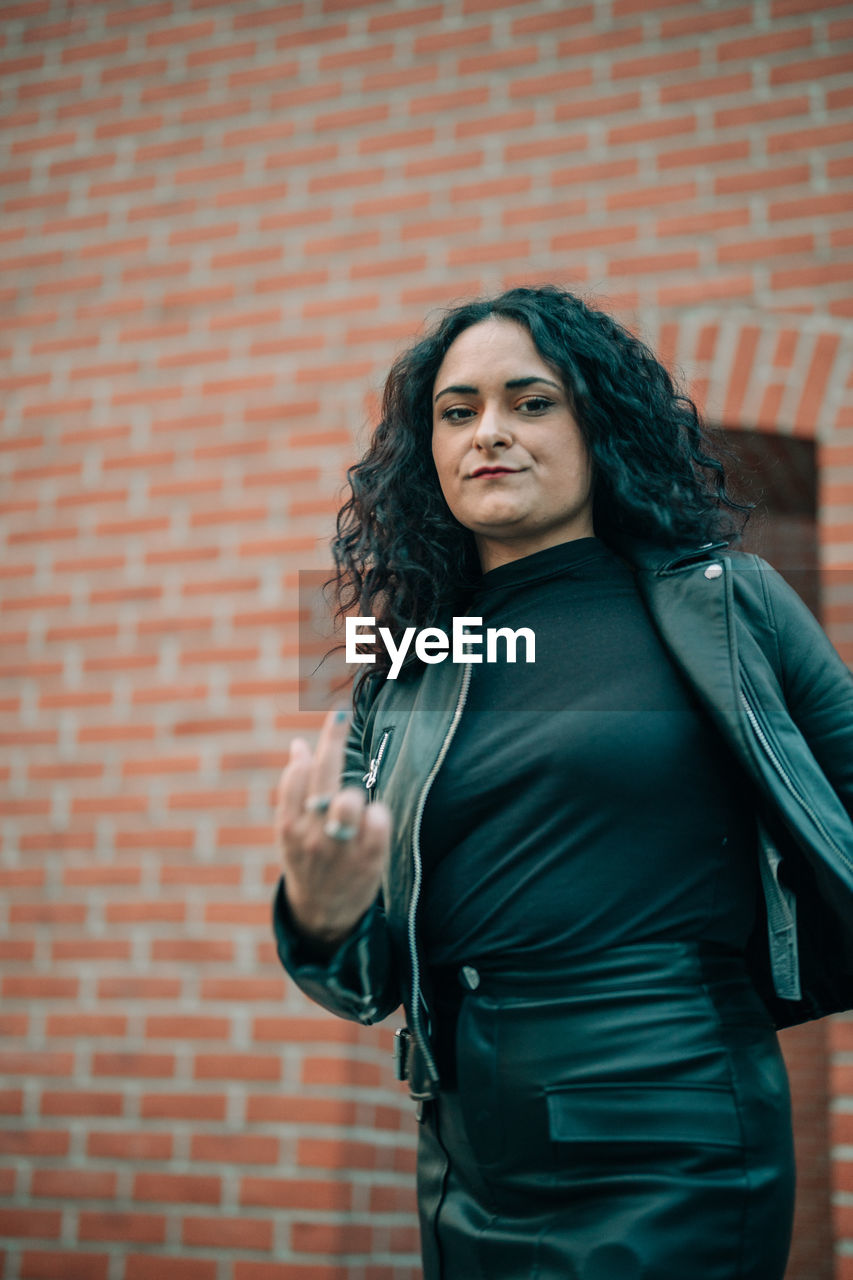 Portrait of woman showing middle finger against wall