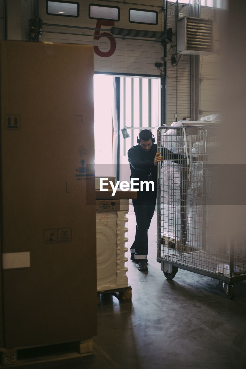 Male manual worker pushing cage trolley at warehouse