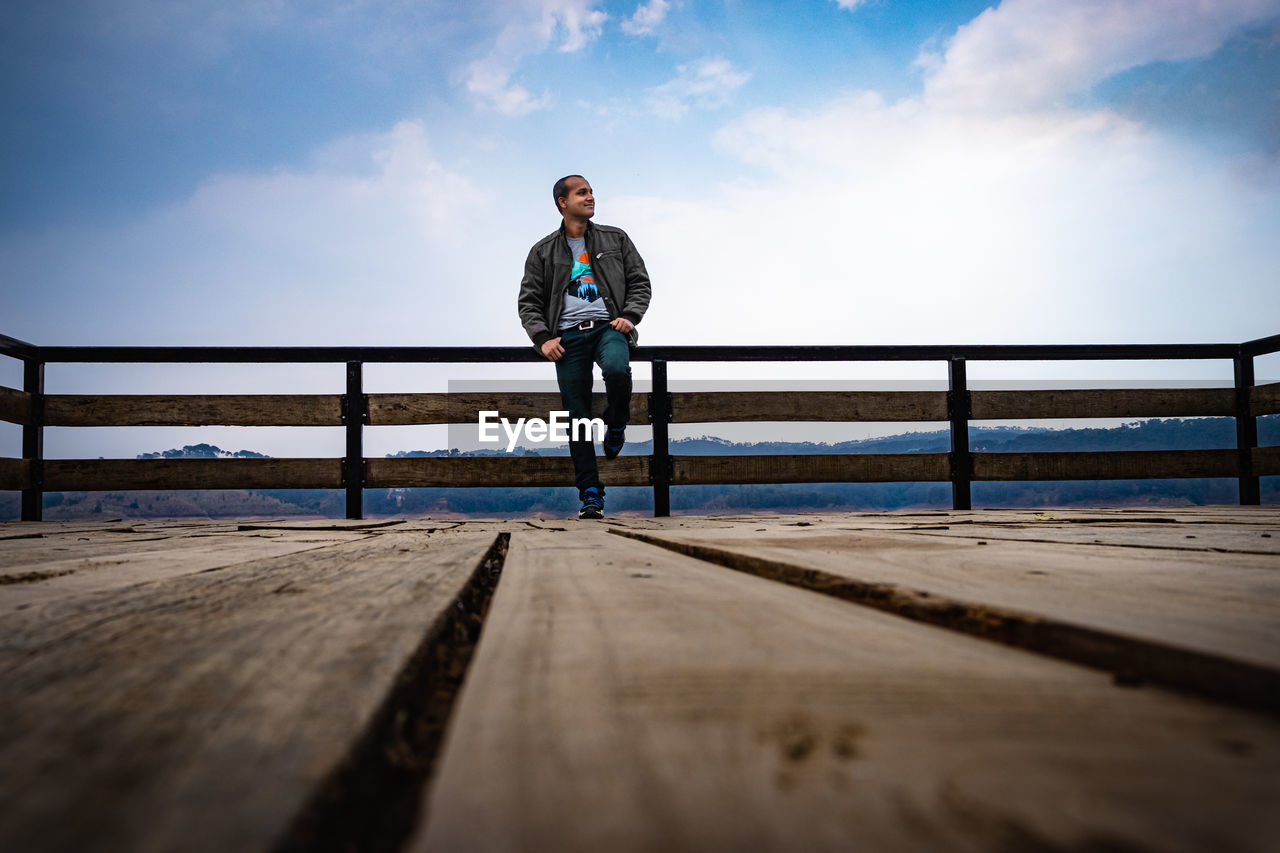 FULL LENGTH OF A MAN STANDING ON RAILING AGAINST SKY