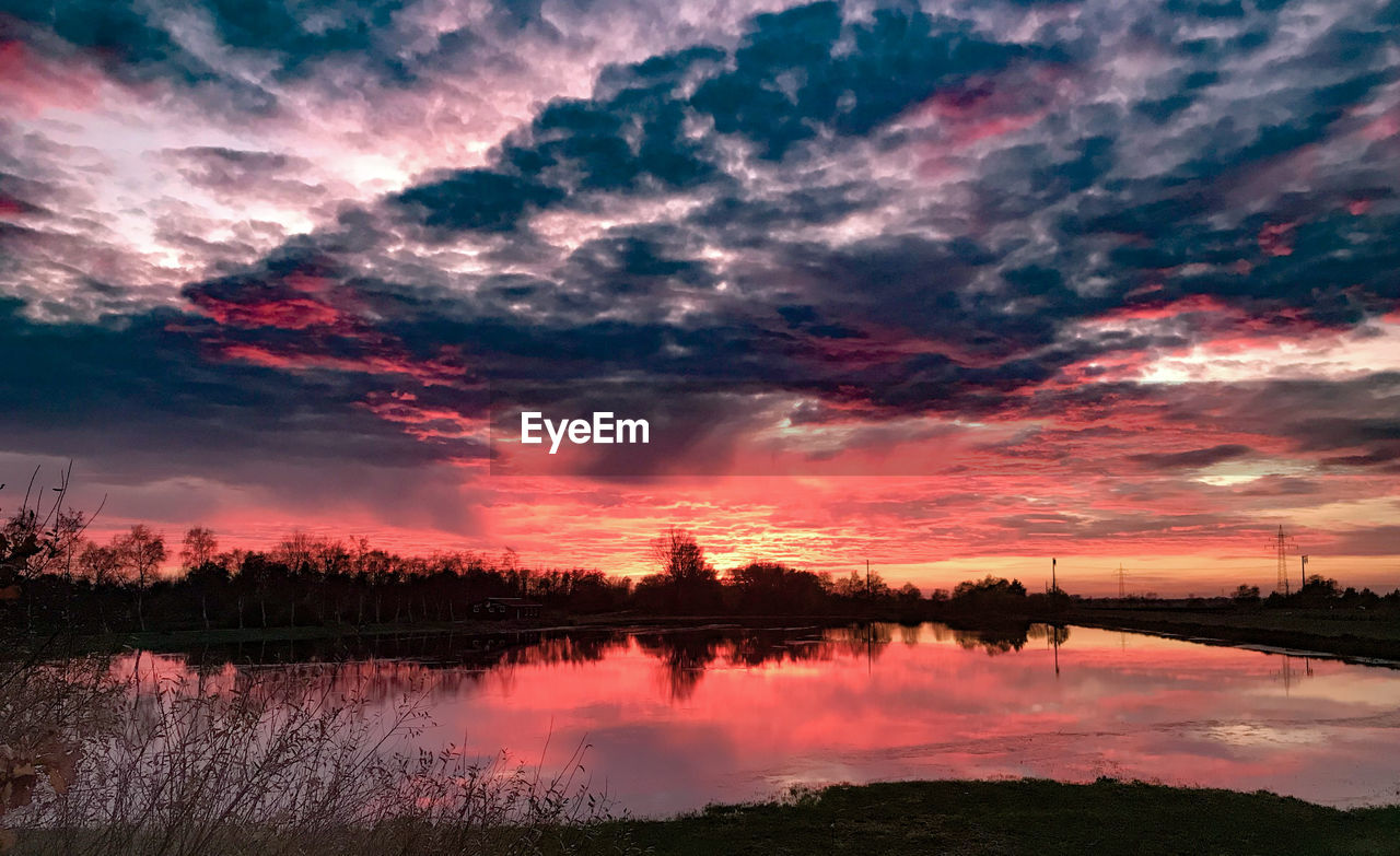 Scenic view of lake against dramatic sky during sunset