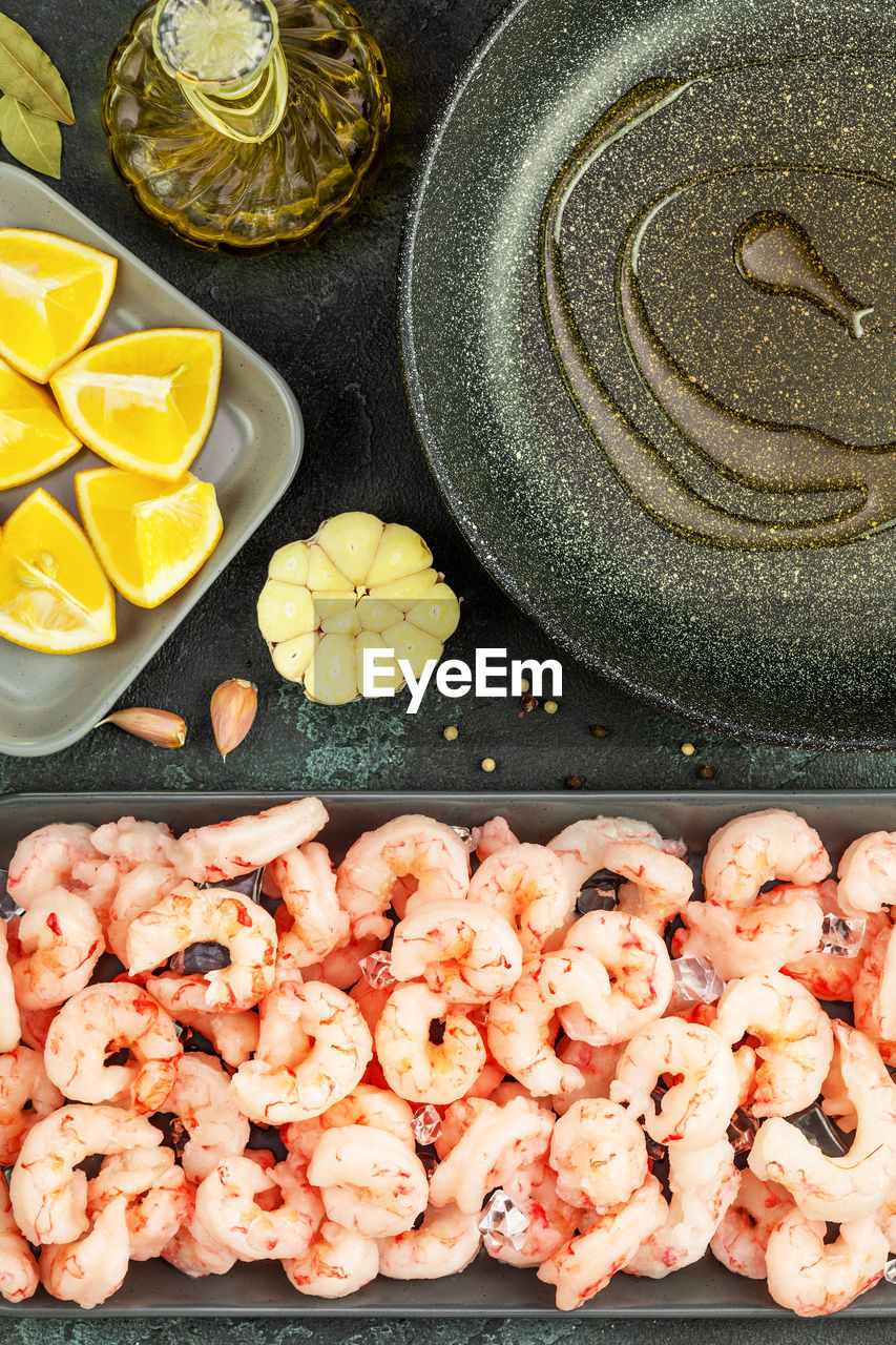 Shrimp cooking. sea food composition with frozen pilled prawns with ice cubes, lemon, olive oil 