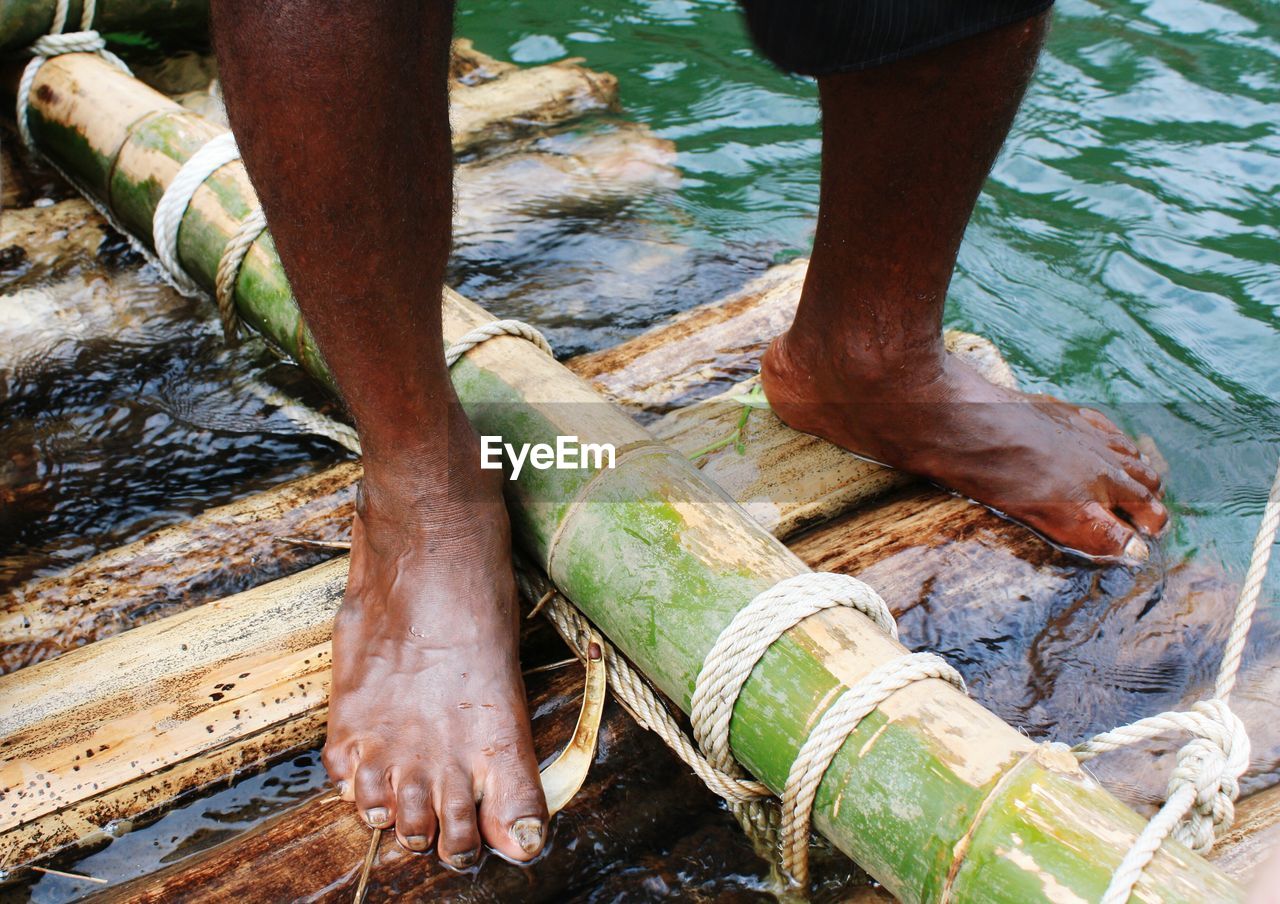 Low section of man standing on wooden raft in river