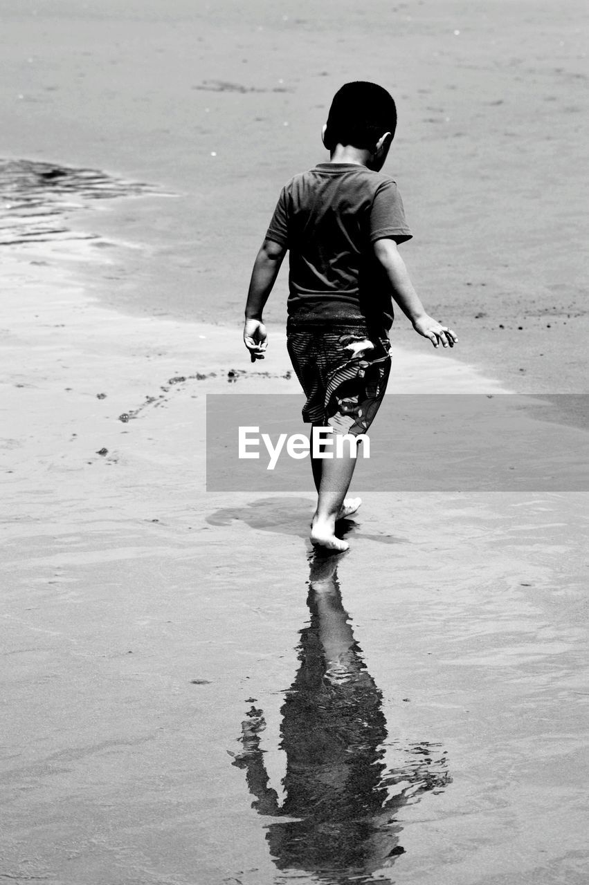 Rear view of boy walking on shore at beach