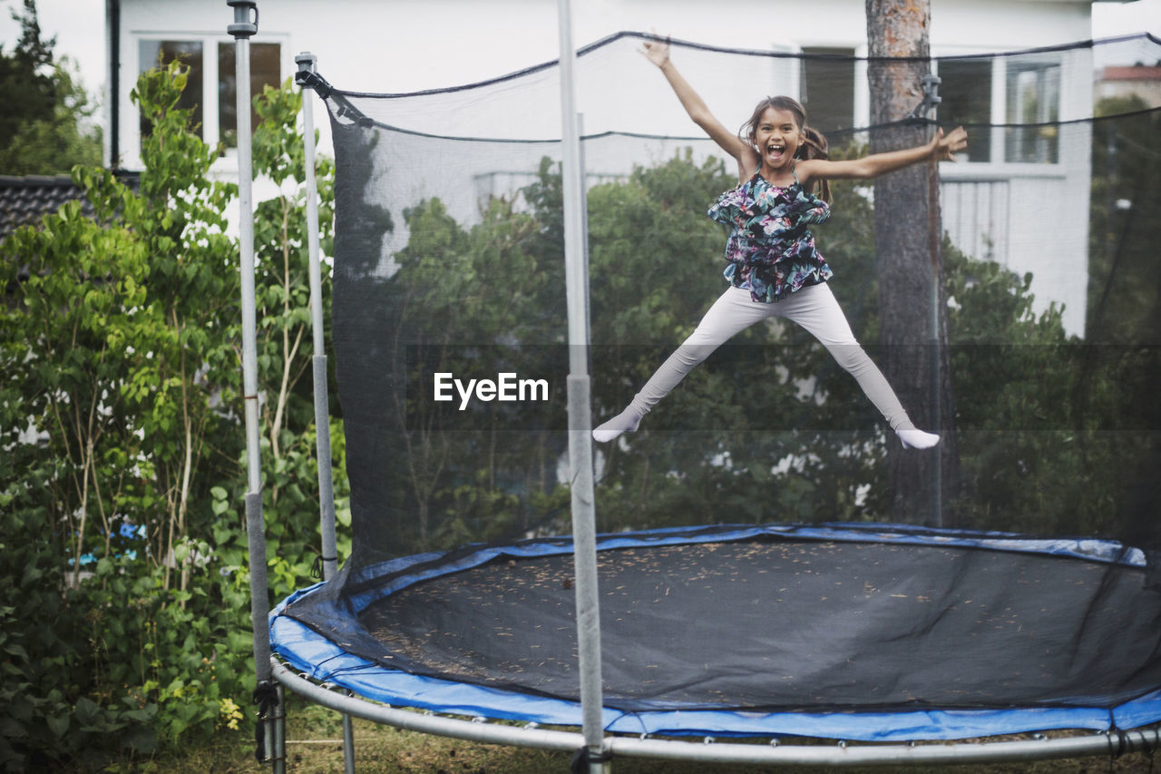 Portrait of excited girl jumping on trampoline at yard
