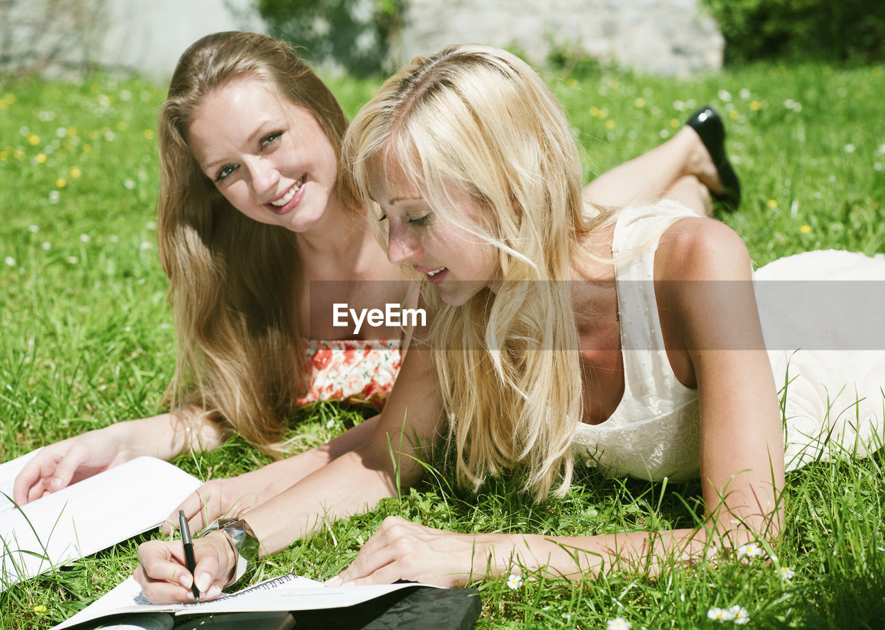 Portrait of smiling woman with friend writing in book at park