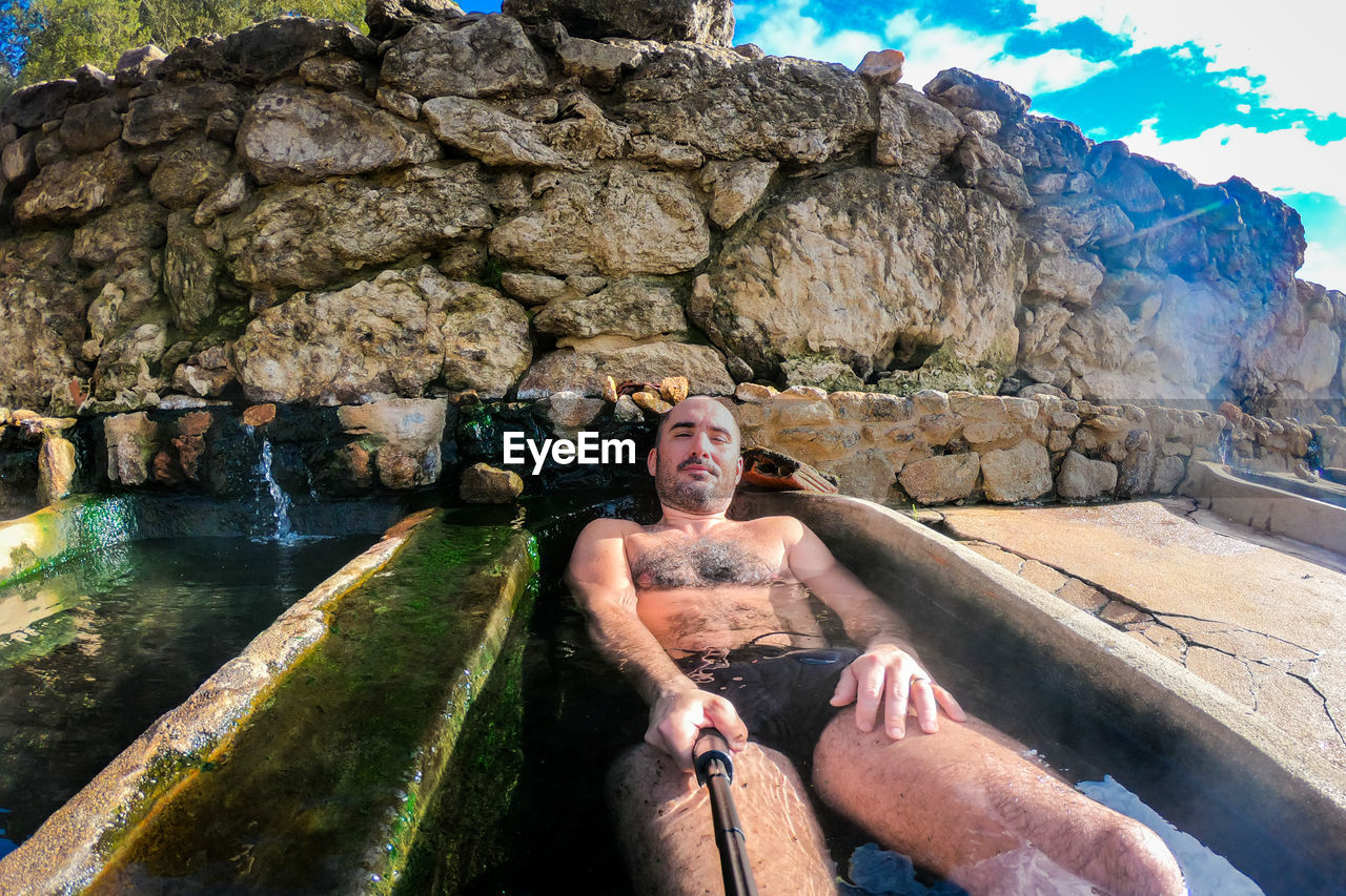 Portrait of shirtless man lying in hot spring