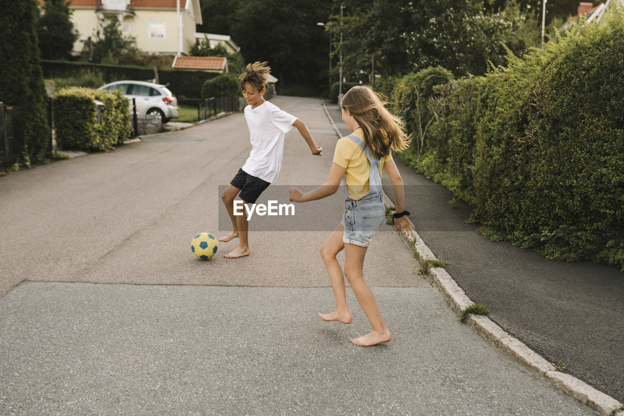 Brother and sister enjoying while playing with soccer ball on road