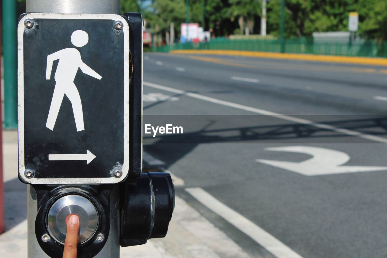 Cropped finger of person pressing button below crossing sign