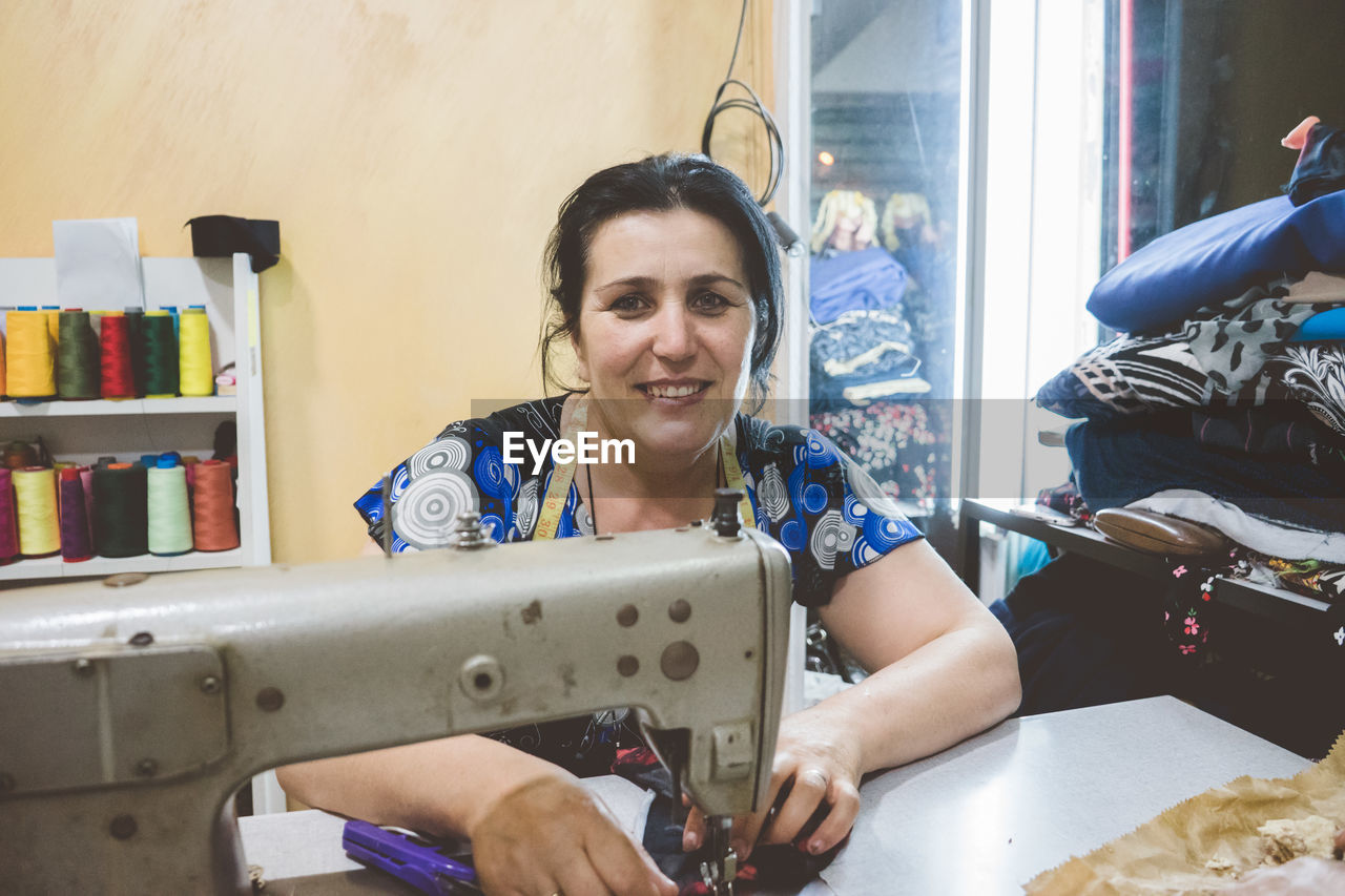 Portrait of smiling woman sewing cloth on machine