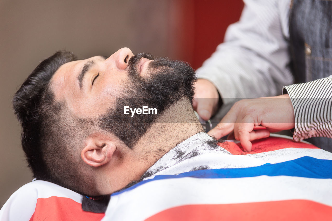 Midsection of barber shaving male customer beard in salon