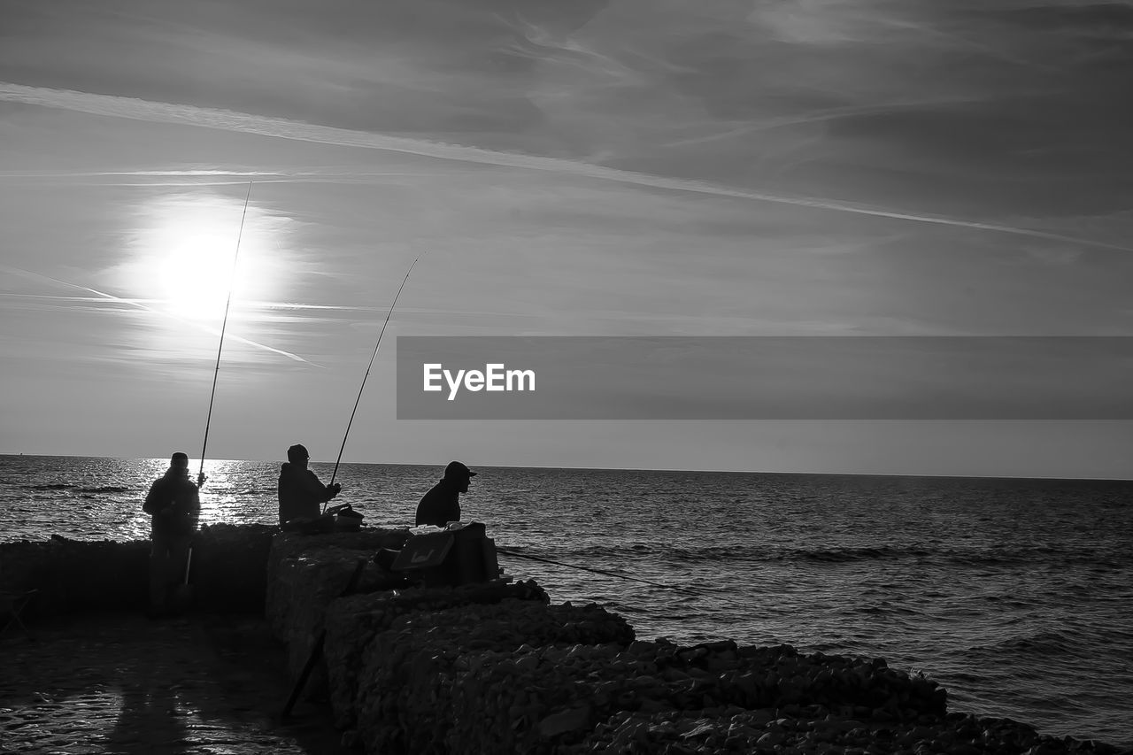 Silhouette men fishing in sea