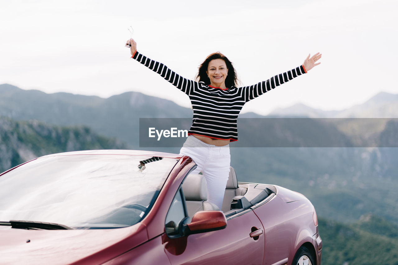 PORTRAIT OF HAPPY MAN STANDING ON CAR