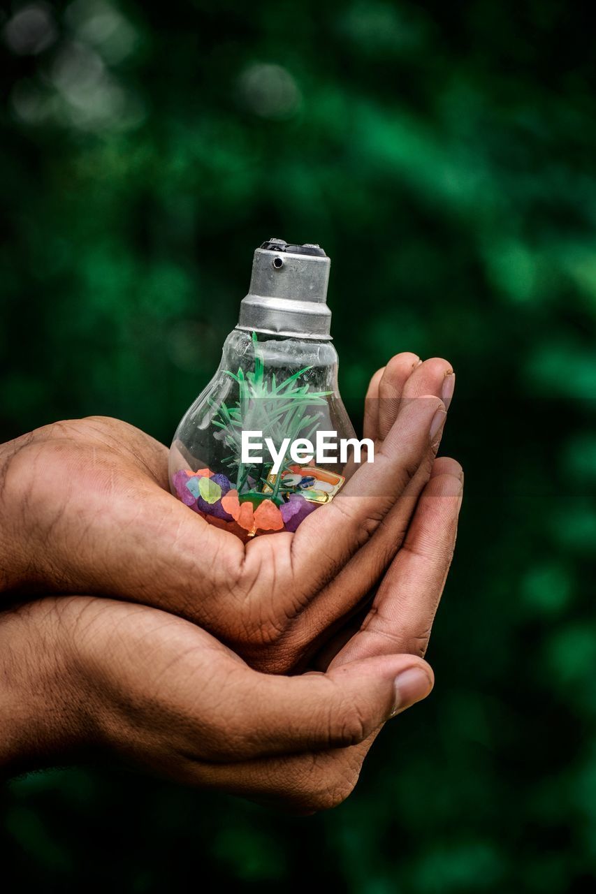 Cropped hands of people holding light bulb with decoration