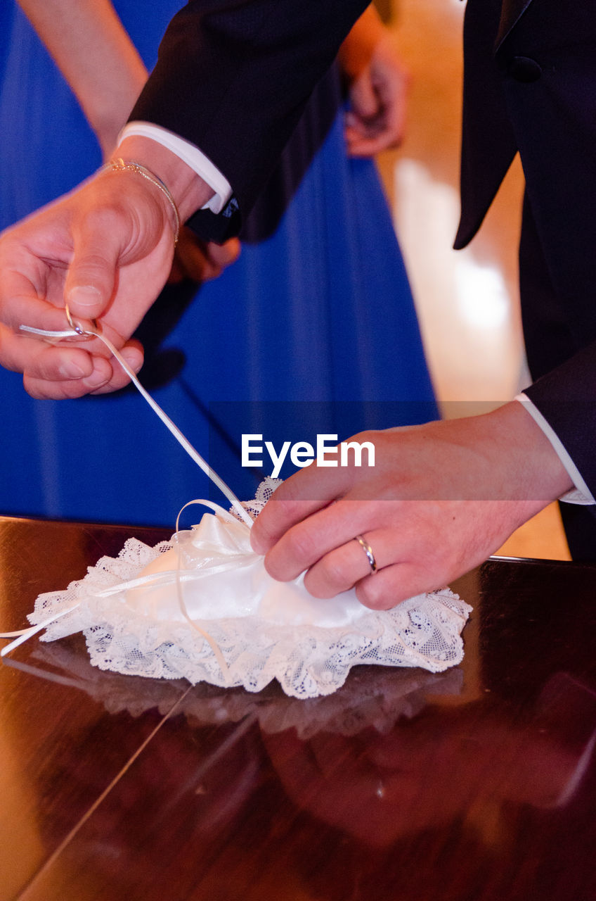 Midsection of bridegroom removing wedding ring from pillow on table