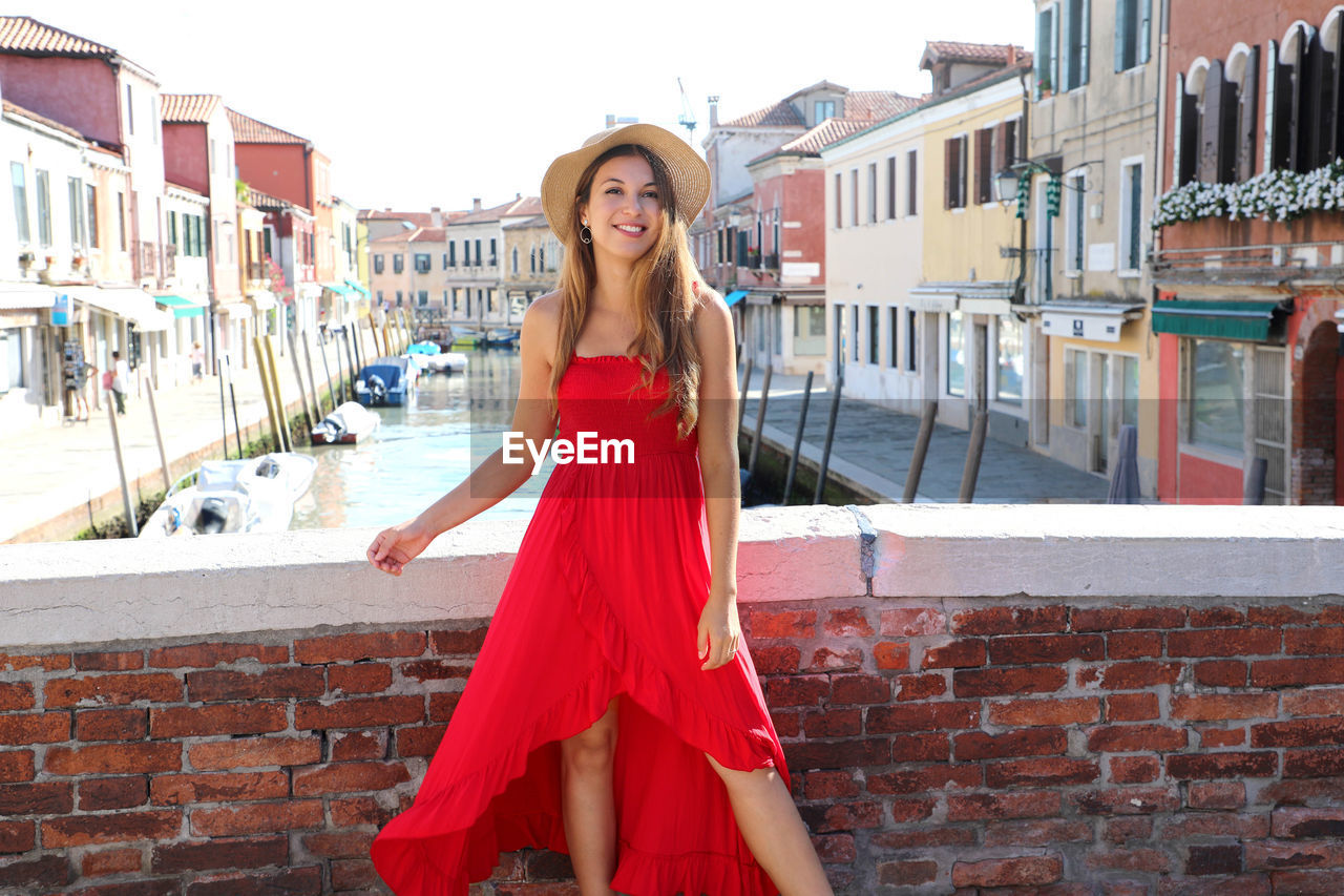 PORTRAIT OF A SMILING YOUNG WOMAN STANDING OUTDOORS