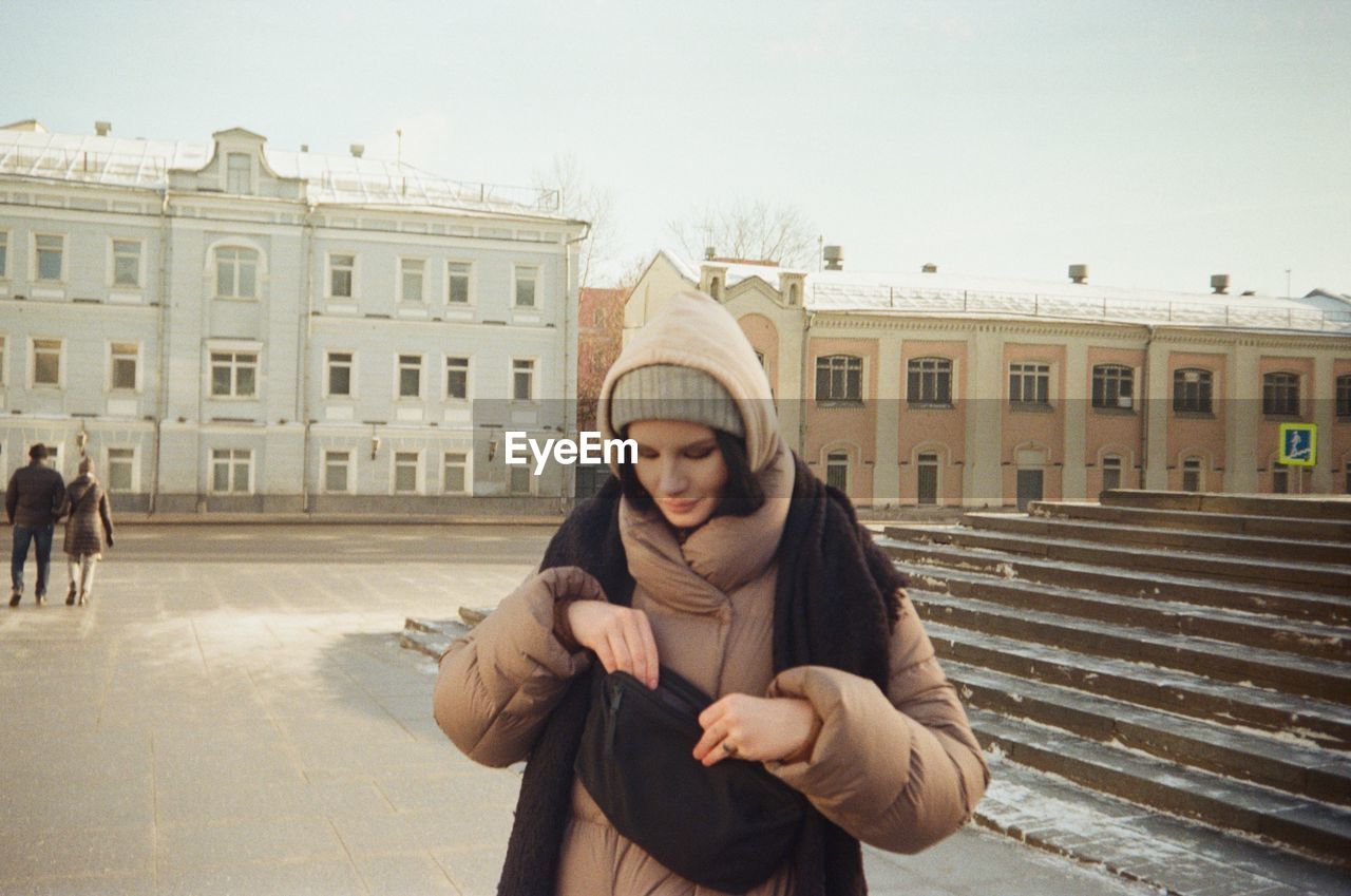 PORTRAIT OF YOUNG WOMAN STANDING IN CITY AGAINST BUILDING