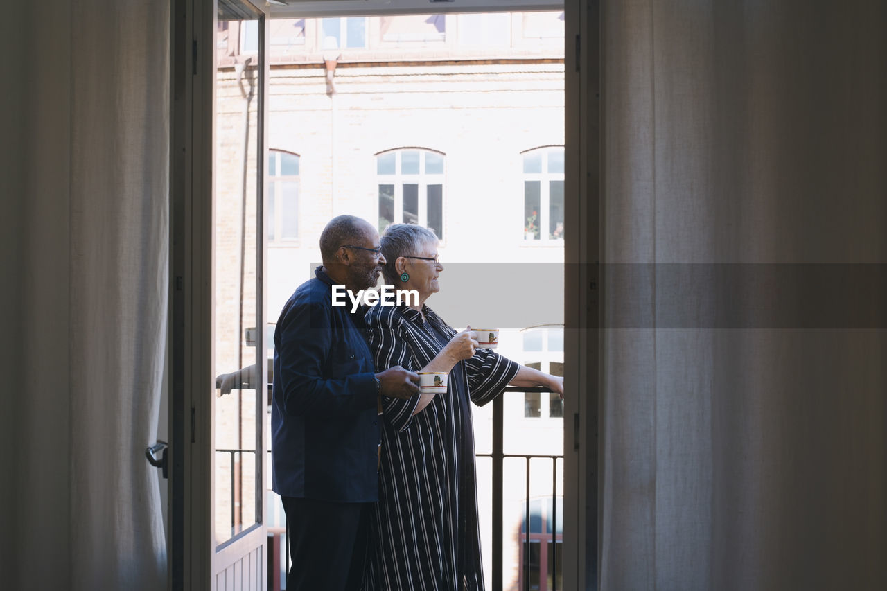 Senior couple with coffee cup standing in balcony at home