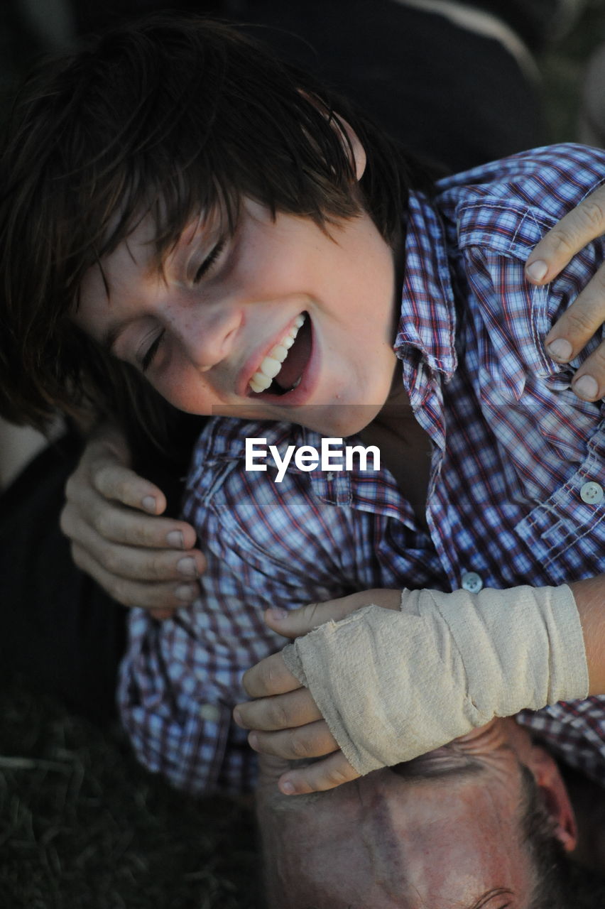 Close-up of cheerful teenager with injured hand falling on father at field