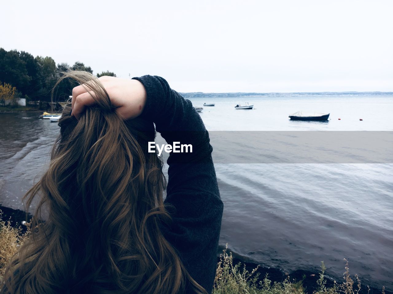 Rear view of woman with hand in hair by sea against clear sky