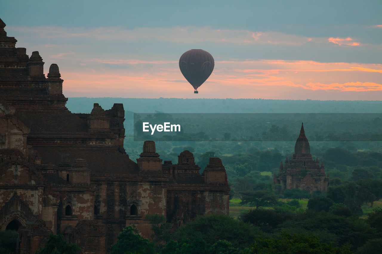 Hot air balloon over temples against cloudy sky at dusk