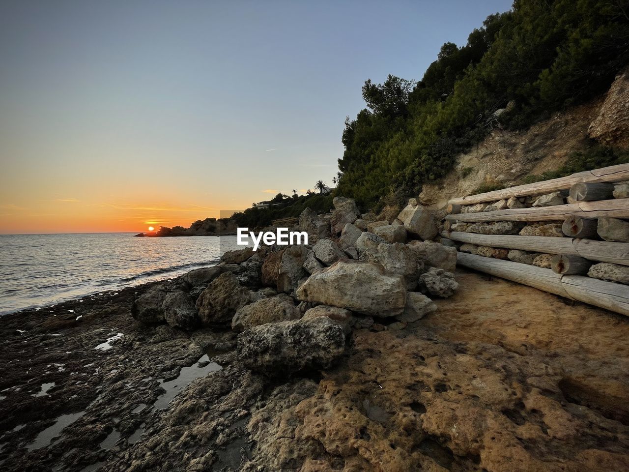 SCENIC VIEW OF ROCKS AT BEACH AGAINST SKY DURING SUNSET