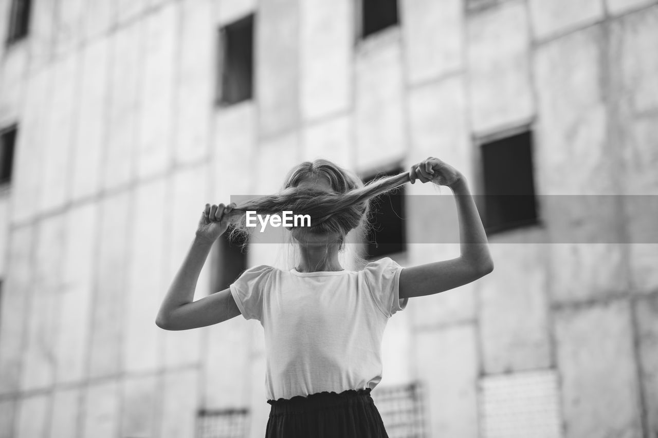 Girl holding braided hair while standing against wall