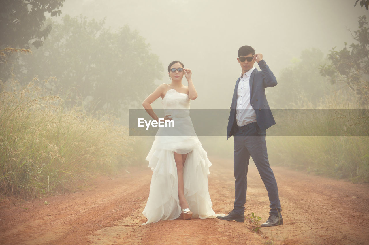 Full length of bride and bridegroom standing on dirt road