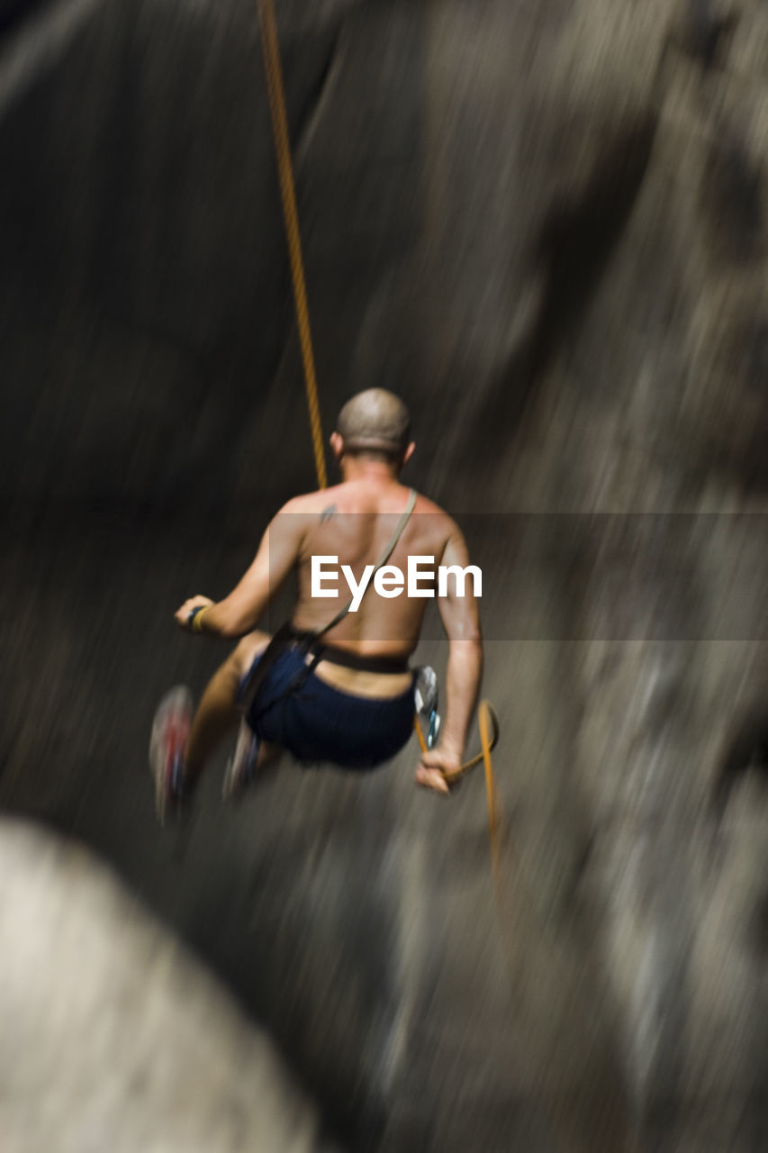Low angle view of shirtless man rappelling on rock formation