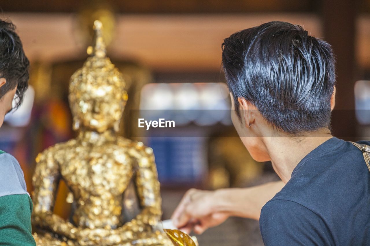 Man sticks gold leaf onto buddha statue