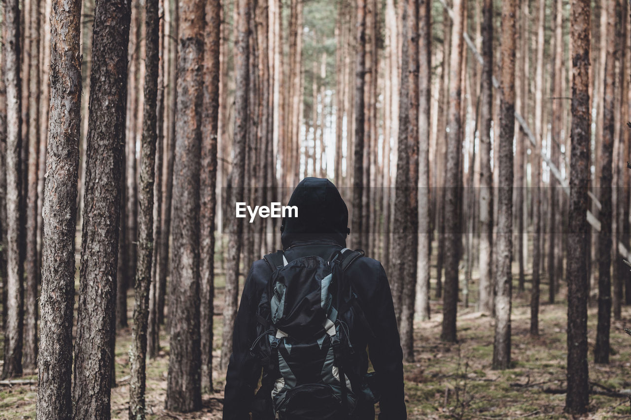 Man in hooded shirt standing against trees