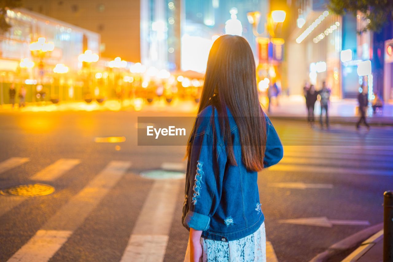 REAR VIEW OF WOMAN IN ILLUMINATED CITY