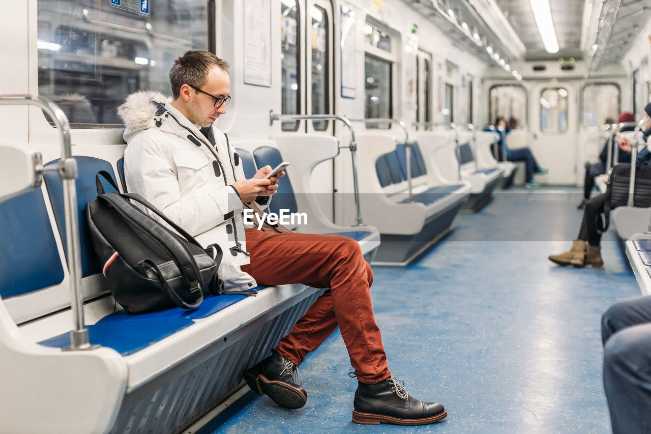 Handsome adult man in glasses riding in subway train. in hands male hold smartphone. copy space.