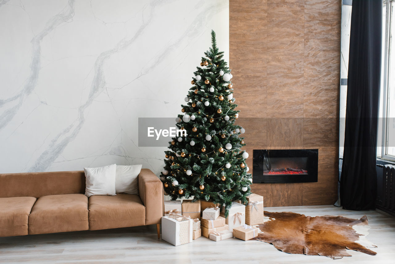 Beautiful christmas tree with gifts near the modern fireplace and sofa in the living room