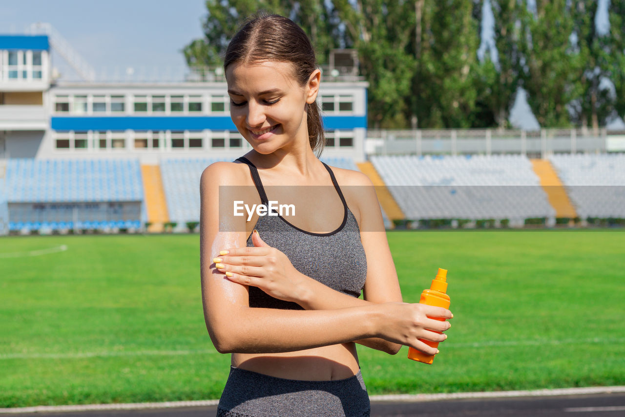 Young athlete applying suntan lotion while standing on sports track