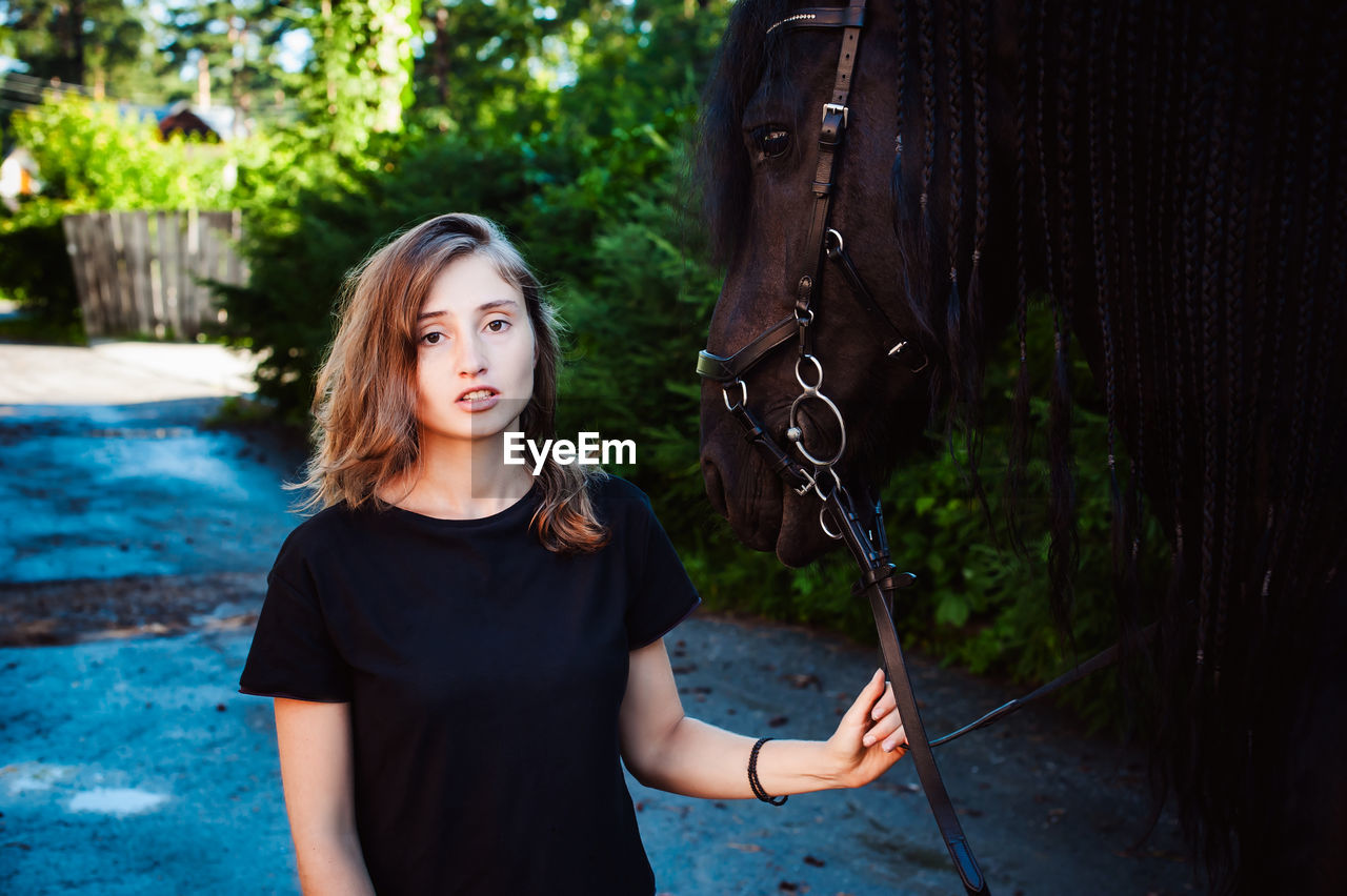 Portrait of young woman standing with horse against trees