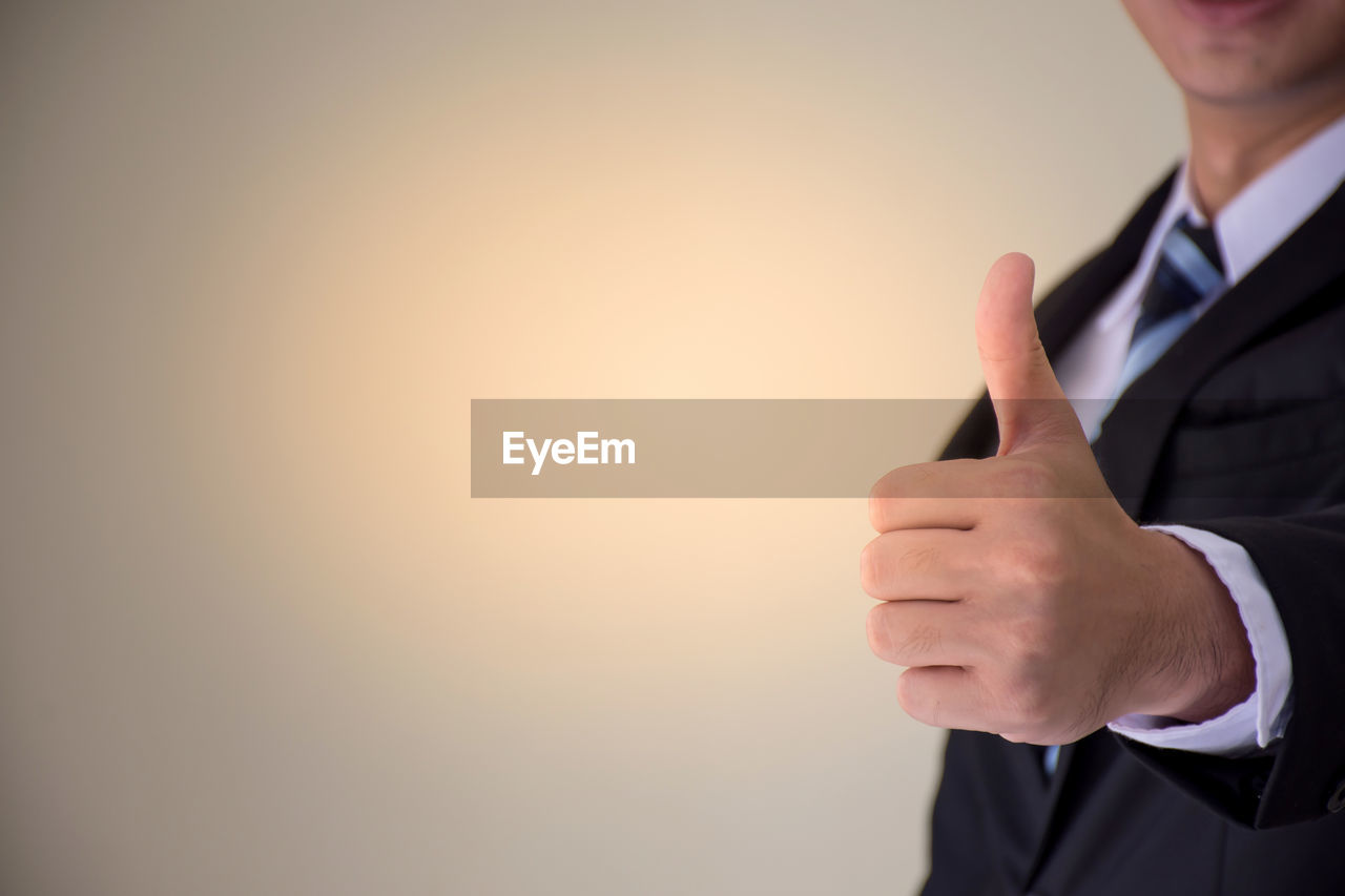 Midsection of businessman gesturing thumbs up against beige background