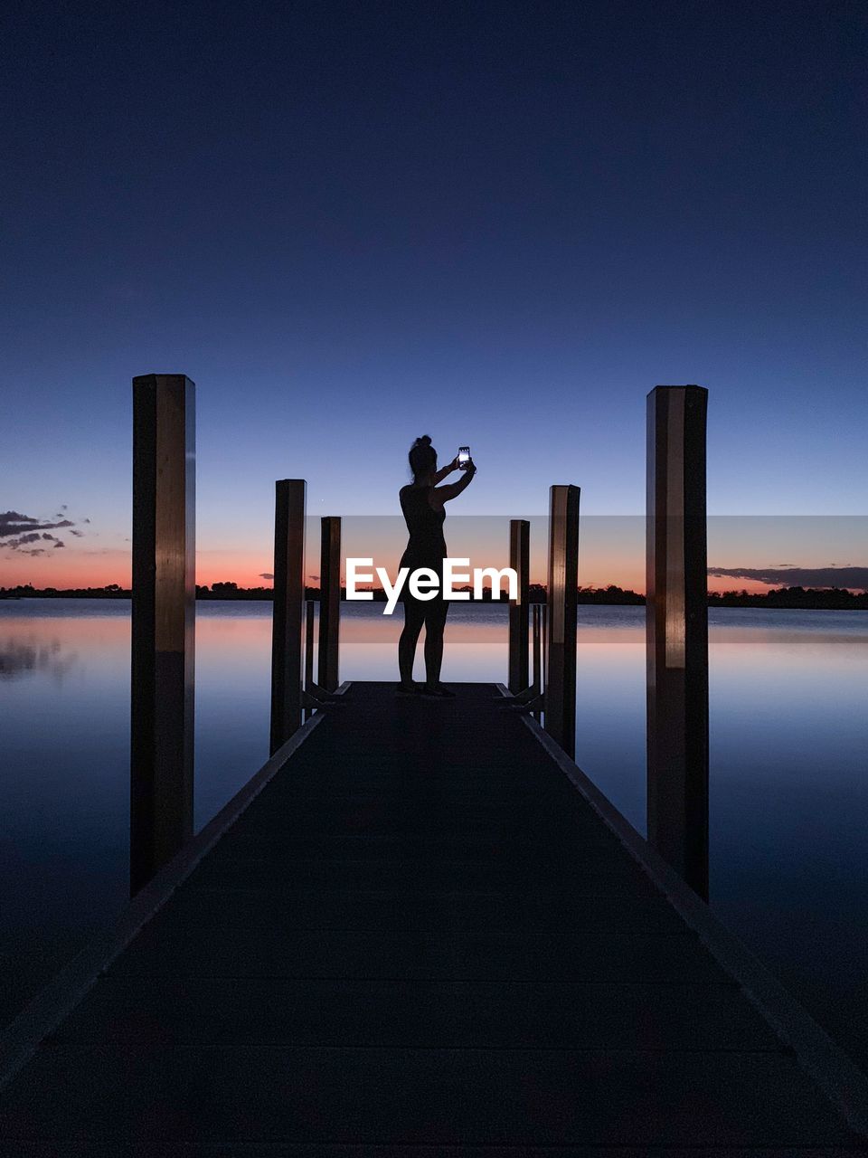 Rear view of silhouette woman standing on pier over sea against sky