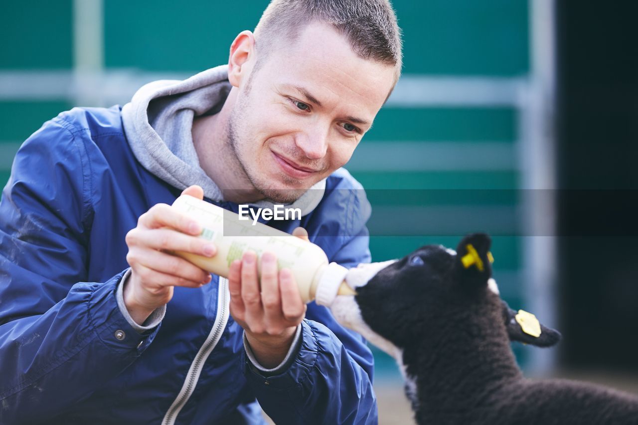 Smiling mid adult man feeding milk to lamb
