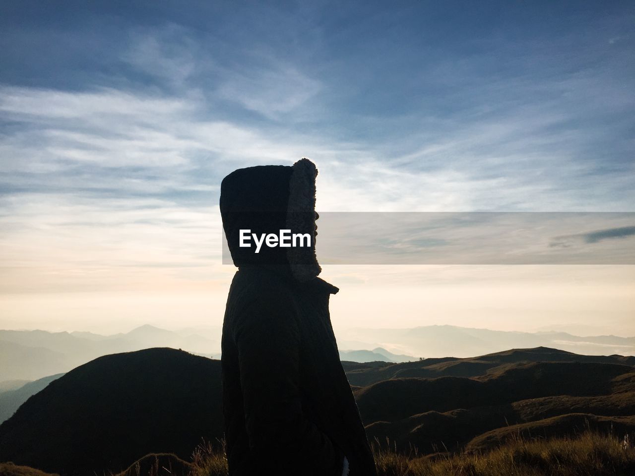 Silhouette of a man behind a scenic view of landscape against sky during sunset