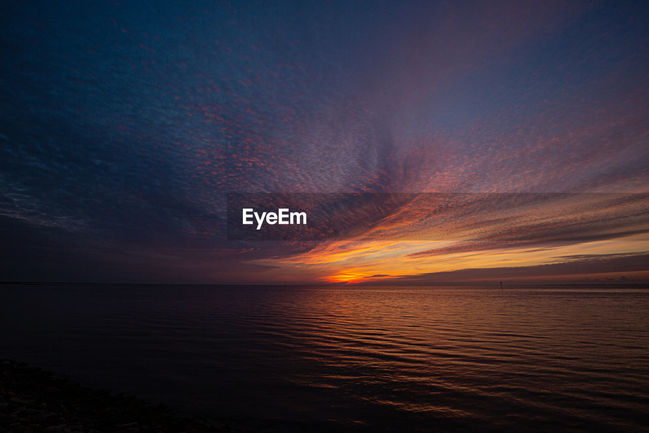 Scenic view of sea against dramatic sky during sunset