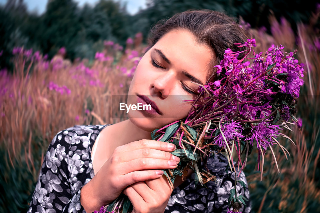 Beautiful woman holding purple flowers against field