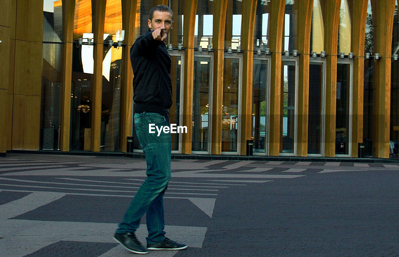 Portrait of young men pointing while walking on street against building