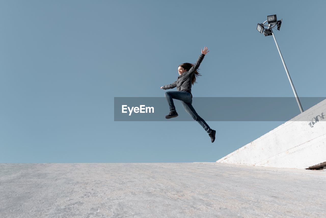 Low angle view of young woman jumping against clear sky