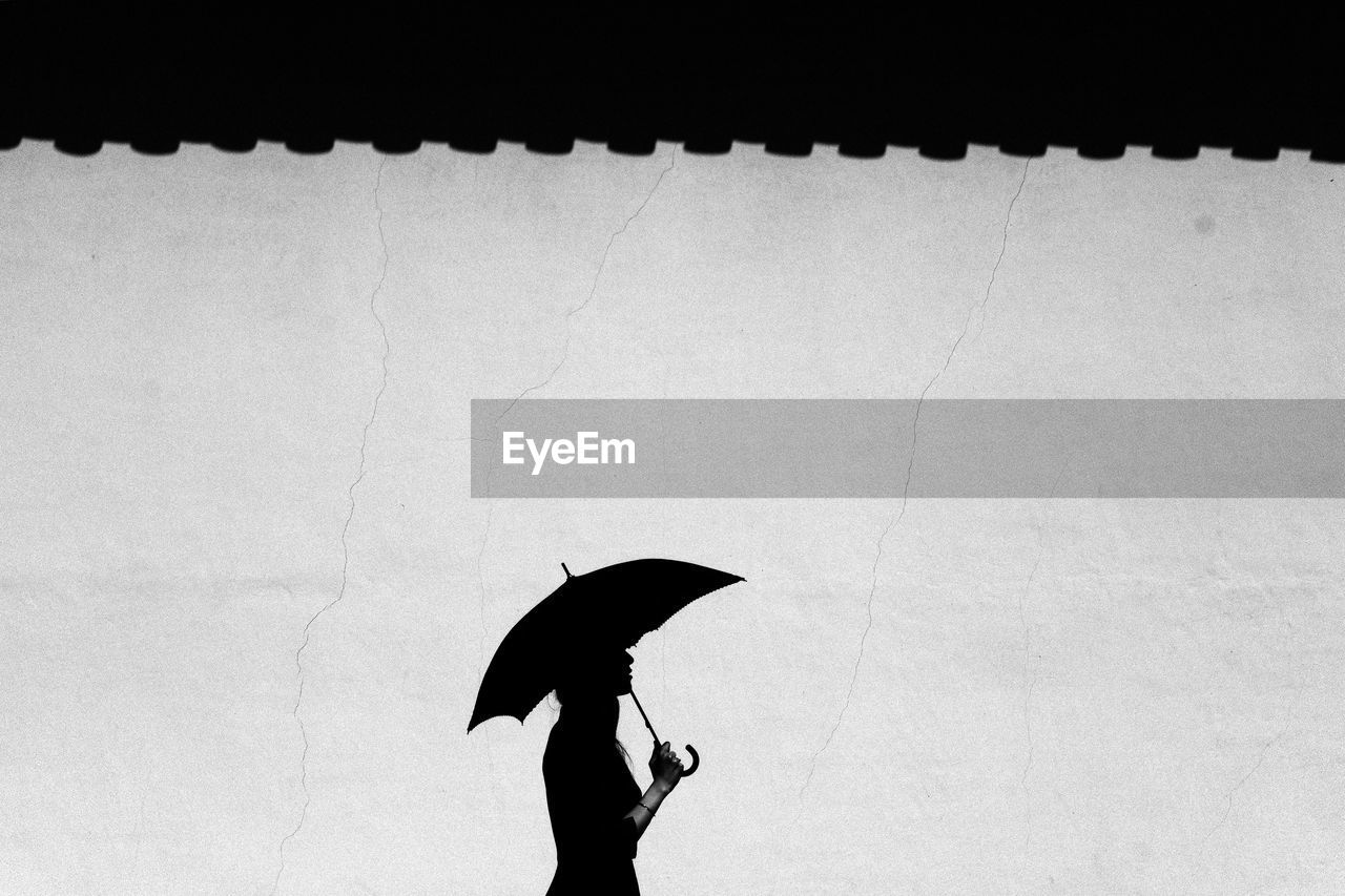 Silhouette of woman with umbrella against wall
