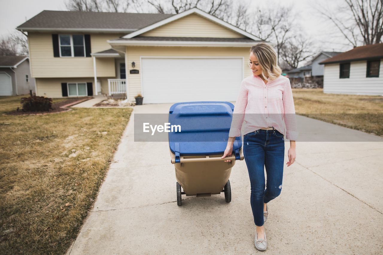 Full length of woman with garbage bin walking on footpath