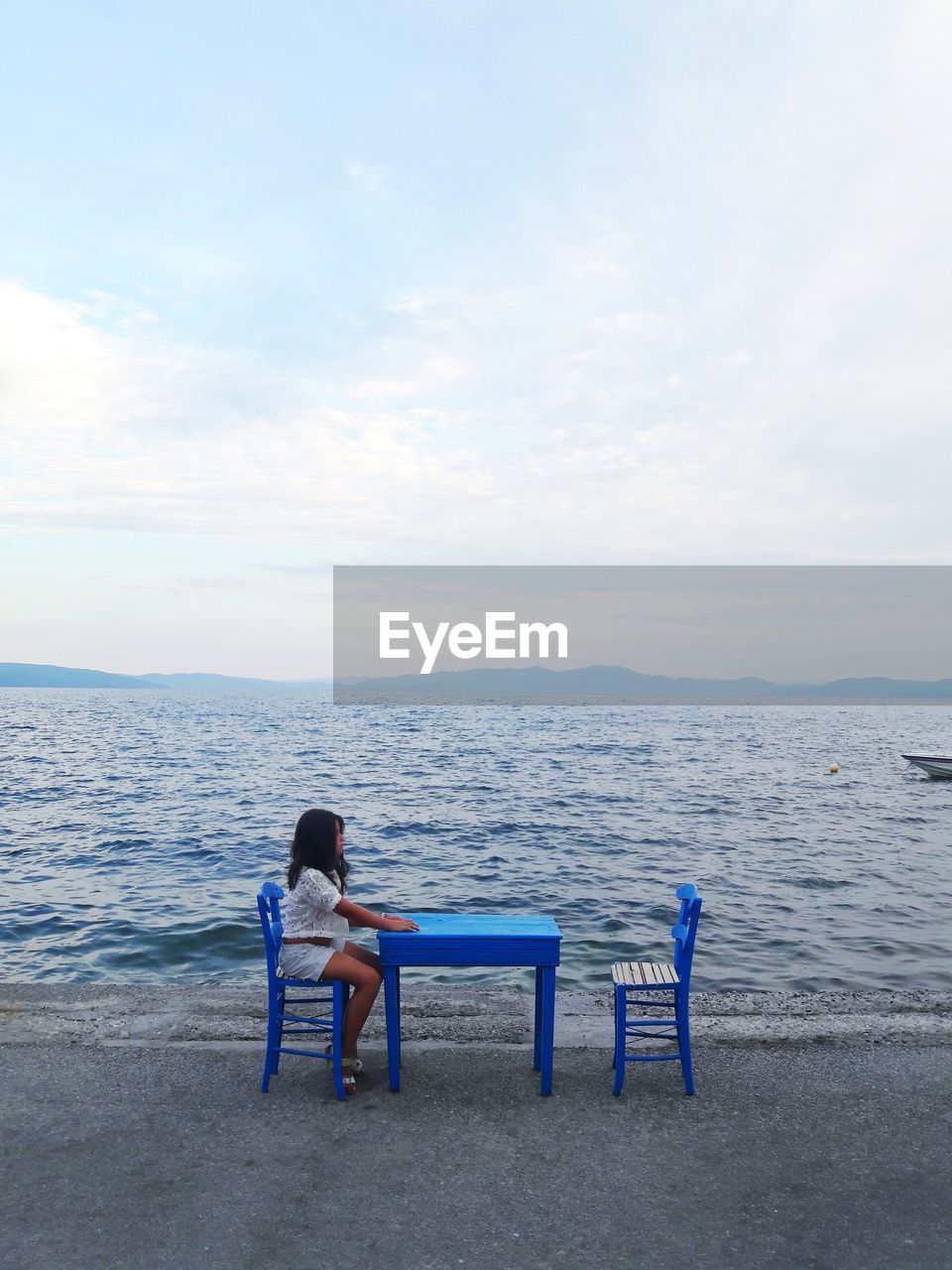 Girl sitting on chair at beach against sky