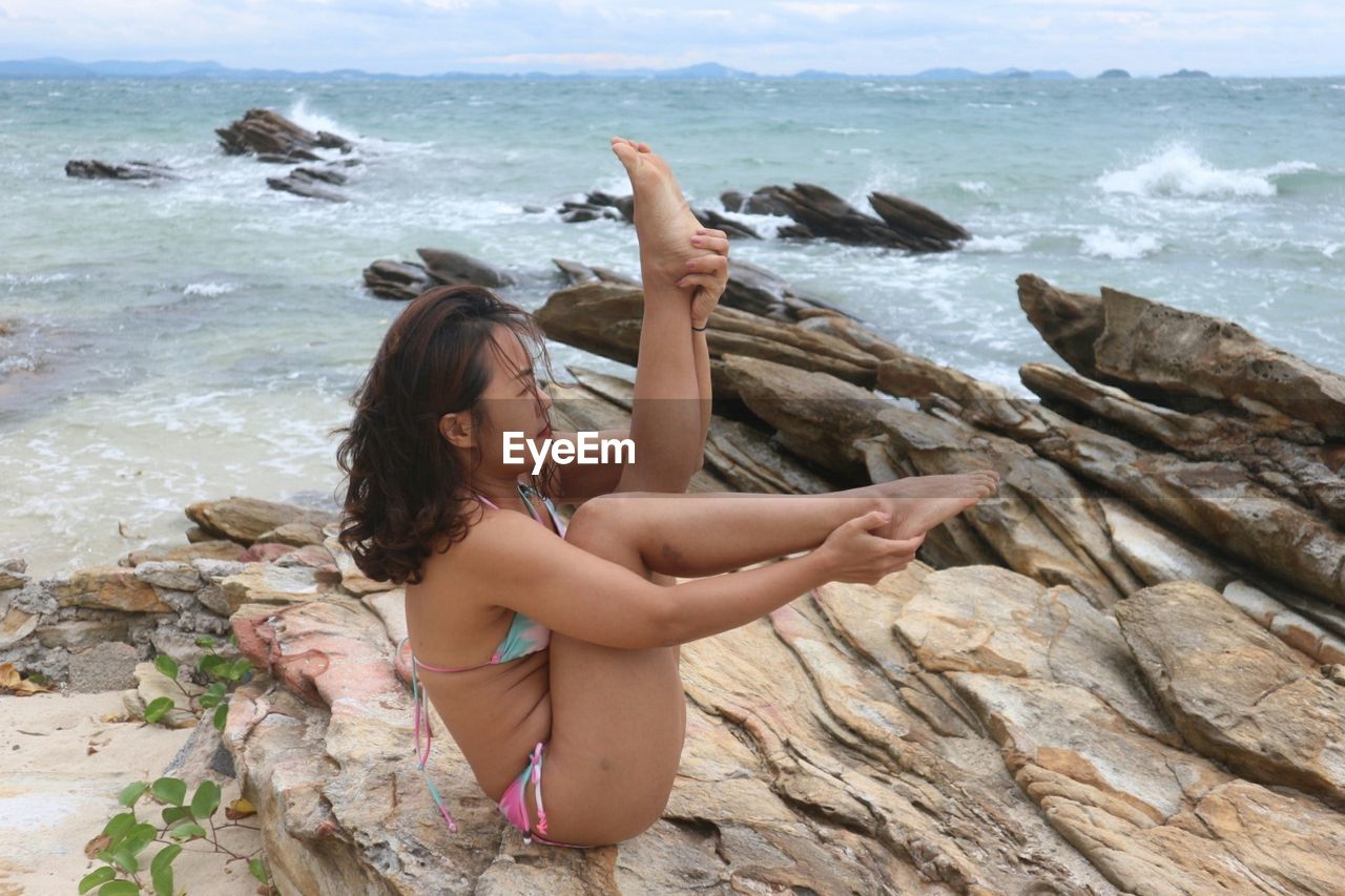 Side view of bikini woman exercising on rock formations